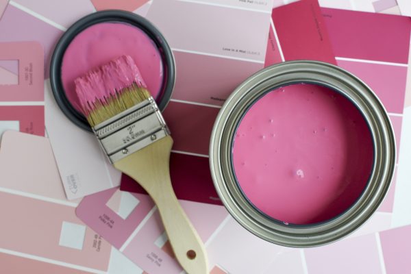 Open can of pink paint with a paintbrush and pink paint swatches